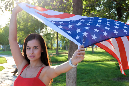 Serious young woman holding american flag flying by the wind