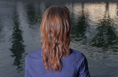Red haired women rear view. She look at view in city park in calm state of mind