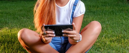 Teenage Girl with tablet computer outdoors cross legged. Young woman is using tablet pc outdoor sitting on grass. Nature background. Copyspace.の写真素材