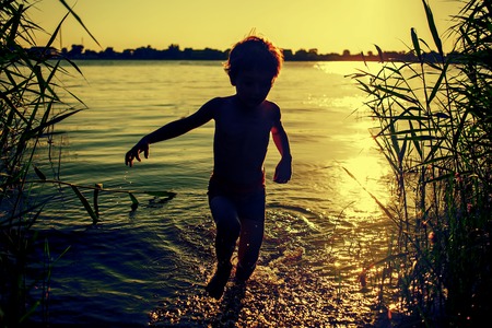 Boy silhouette running out of water on the beach at sunset.