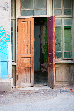 Old wooden door open of a shabby demaged house facade or front in brown, green and turquoise colorsの写真素材
