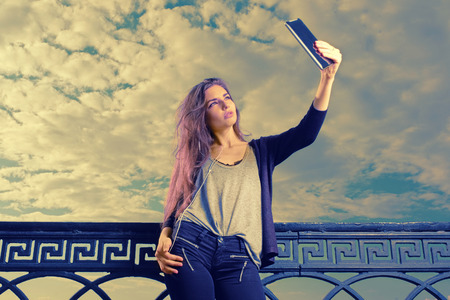 Pretty young female fashion model takes travel selfie at sky with clouds backgroundの写真素材