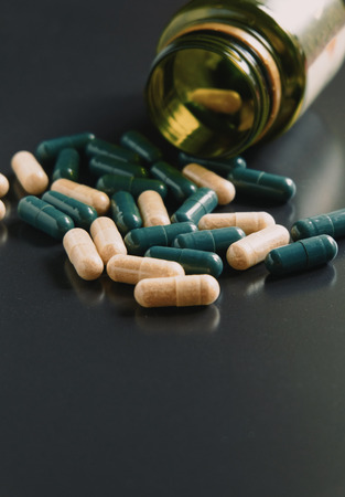 Closeup of medical capsules or pills of drug. A lot of two-color pills spill out of bottle on black background. Vintage color tone.の写真素材