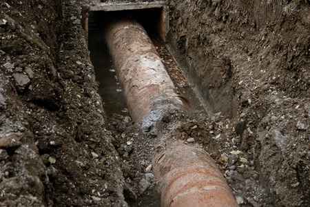 Rusty water pipeline in the trench ground overhead view. Repairing of the water delivery system. Open trench with water pipe in a ground. Industrial plumbing of outdated conbstruction..の写真素材