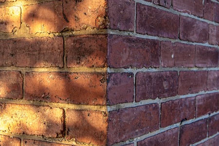 Corner of dark red brick wall with shadows and a lot of space for text.の写真素材