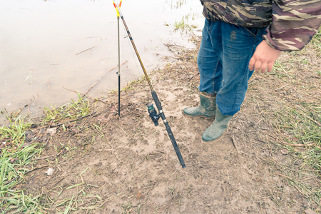 Modern fishing rod outdoors on the ground and fishermans legs above view.