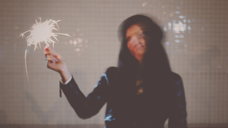 Blurred in motion image of young woman dancing with burning sparkler in her hands in the night city...