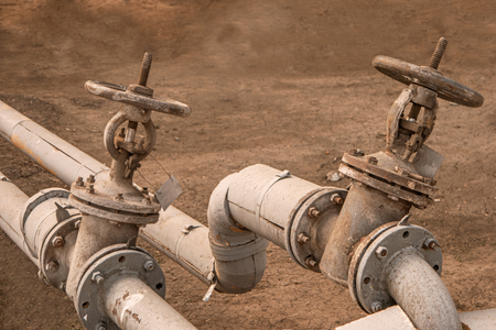 Two worn looking hot water valve mounted on pipes outdoors, shot with copyspace. Old water faucets....
