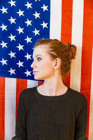 Young gender fluid girl looking away in front of US stars and stripes flag vintage color.の写真素材