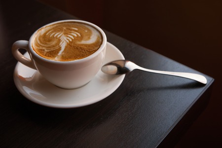 Cup of cappuccino on sourcer with spoon standing on the corner of table, vintage warm color.の写真素材