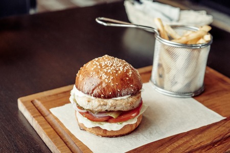 Chicken burger with tomato served on piece of paper on a rustic wooden plate in street cafeの写真素材