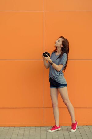 Full Body portrait of a beautiful girl with old film camera looking up on orange wall backgroundの写真素材