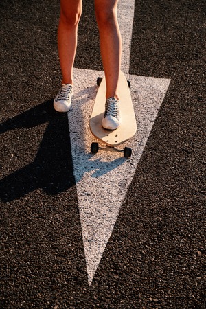 Skater girl is ready to start moving forward, aiming concept. Legs of skater tteen standing on arrow road marking in ready to ride position.の写真素材