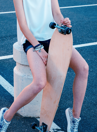 Girl-skater sitting in skate park with her longboard between her bare legsの写真素材