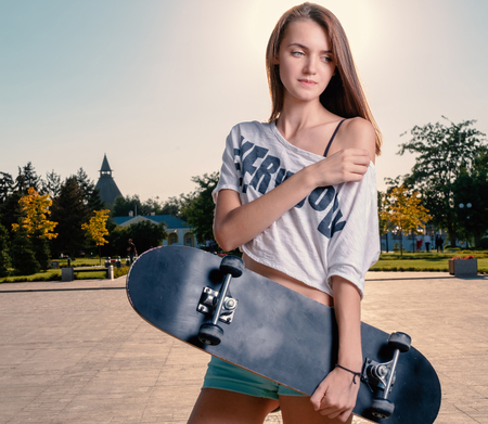 Long haired girl holding skateboard posing with bare shoulderの写真素材