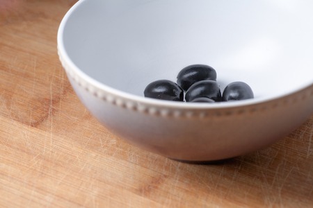 Bowl with some black olives side view. Copyspace on the wooden plate. Diagonal composition, part of the bowl.の写真素材