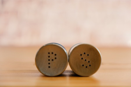 Metal pepper shaker and salt shaker lying near each other on wooden tableの写真素材