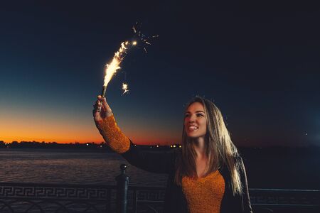 Happy woman with burning sparkler in raised hand raised in front of dark night sky with copyspace
