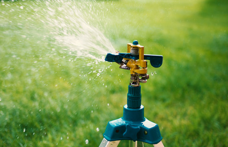 A garden sprinkler mounted on a tripod watering new grassの写真素材