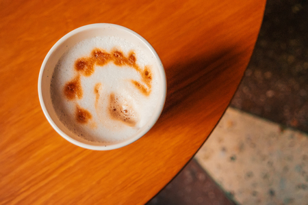 Top view of freshly made cup of cappuccino with abstract latte art standing on the edge of round coffee tableの写真素材