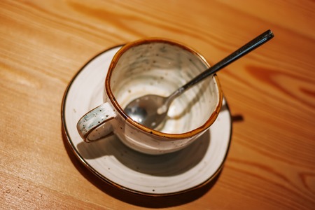 Empty ceramic cup on wooden table with silwer spoon inside