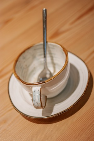 Empty ceramic mug on wooden table with silver spoon insideの写真素材