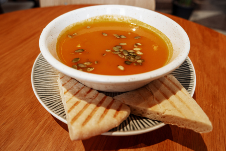 Seasonal autumn pumpkin cream soup puree with pumpkin seeds and two pices of pita breadの写真素材