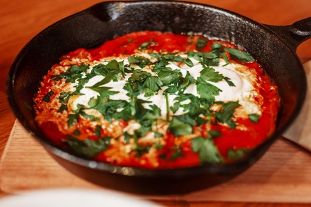 Shakshuka Served in a Frying Pan Angle View. Eggs Poached in Spicy Tomato Pepper Sauce In Cafeの写真素材
