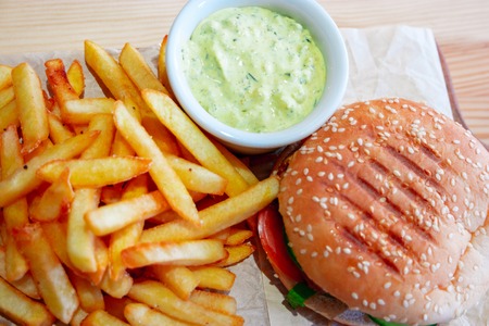 Tasty Grilled burger on cutting board with french potato fryes on wooden rustic background above...