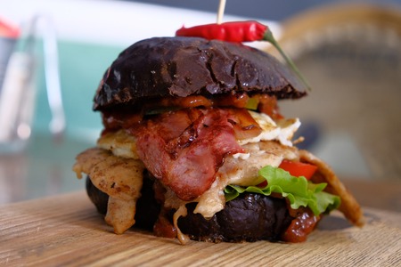 Side view of Big messy burger served on chopping board with red pepper on the topの写真素材