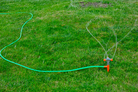 Sprinkler system watering the backyard with blurry waterdrops flying in an air and hose lying on green grass with copyspace.の写真素材