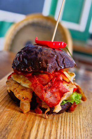 Burger with hotpepper on top served on wooden boardの写真素材