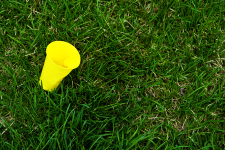 Yellow plastic cup lying over fresh green grass. Environmental issues - plastic contaminates our common homeplanet Earthの写真素材