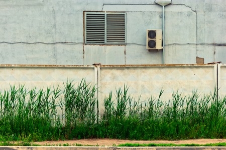 Industrial buiding with air conditioning system situated behind concrete wall with reed grows in front ofの写真素材