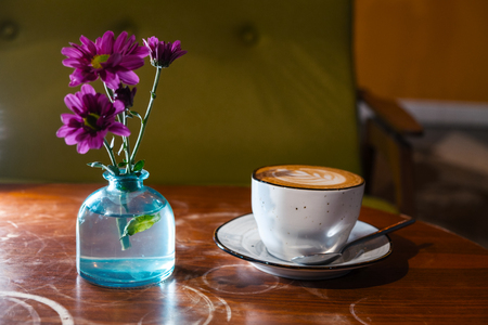 Cappuccino cup on table wih flowers in blue bottleの写真素材