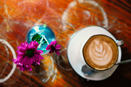 Cappuccino coffee cup on table wih flowers in blue bottle top viewの写真素材
