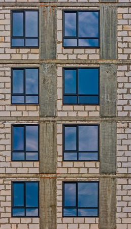 Wall of modern apartment building with just-mounted windows with sky reflection vertical image.の写真素材