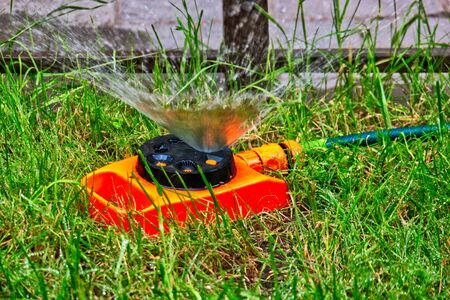 Garden sprinkler of orange color working on lawn with fountain of water drops flys in an airの写真素材