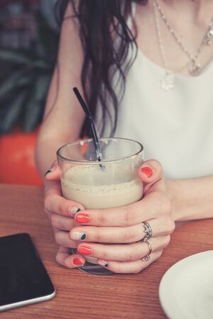 Woman sitting at a table in a cafe with a cup of coffee between her handsの写真素材