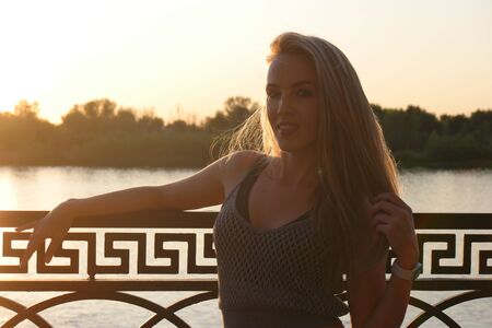 Portrait of happy woman standing outside on waterfront in sunny summer or spring day sunshine. Sporty adult smiling woman looking at you, attractive young girl enjoying summertime, backlit image full of sunlightの写真素材
