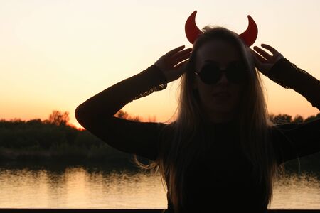 Close-up portrait of a horned female in sunglasses on waterfront in sunsetの写真素材