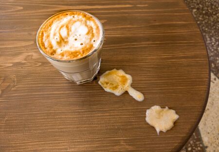 A glass of flat-white coffee stands on the table and next to the visible spilt milk, the view from aboveの写真素材
