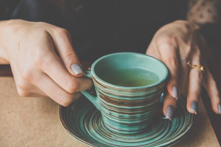 Women's hands hold a green ceramic cup with a creative Japanese-style pattern. Image in vintage retro styleの写真素材