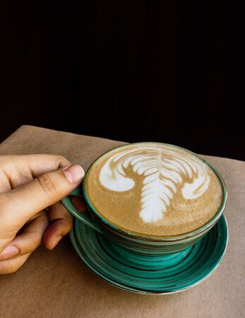 There is a cup of cappuccino on Kraft paper and it is held by a mans handの写真素材