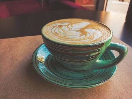 A large cappuccino cup of green color stands on a table covered with Kraft paper. Toning imitates an old film photo.の写真素材