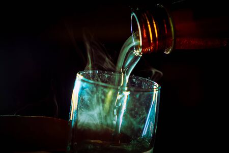 The bartender, or maybe Satan himself, pours a steaming green toxic liquid into the glass. Alcoholism and bad habits, sinful behavior concept.の写真素材