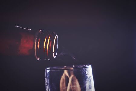Open bottle neck hanging over the shoot glass in the dark and light smoke is flying about. Copyspace.の写真素材