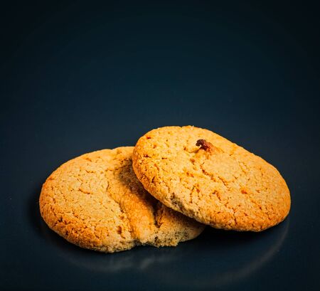 Two oatmeal cookies lie on top of each other and one of them is bitten. The photo is on a black...