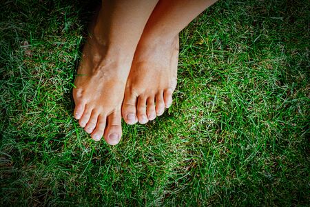 Feet on grass shot from above. Image with copyspace and vignette. Soft tender bare feet are set on...
