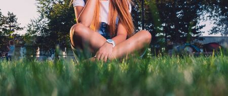 Teen girl is sitting cross-legged on grass grown level view with copyspace and blurred grass on foregroundの写真素材